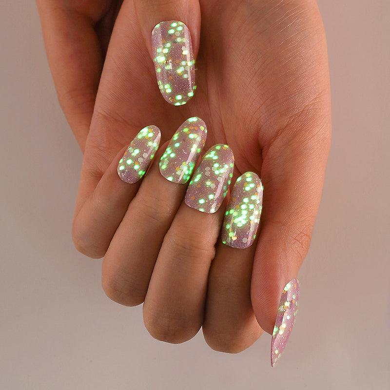Hand with glow-in-the-dark gel nails emitting a soft green luminescent glow against a dark background.