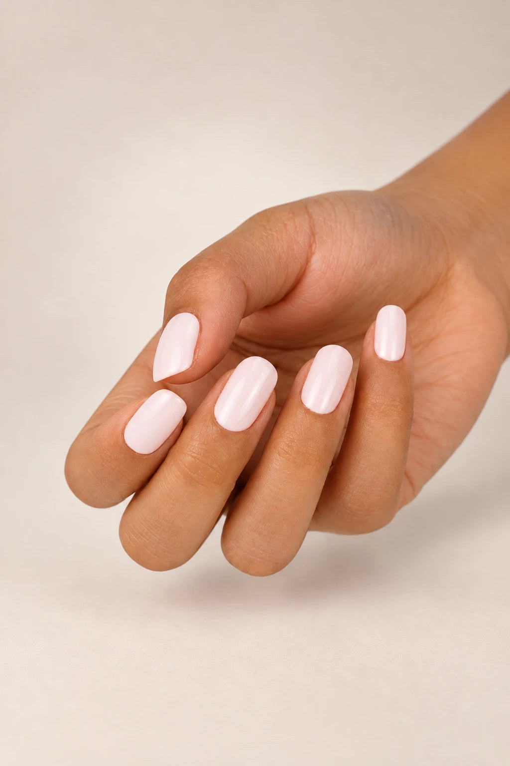 Close-up of a hand with short, glossy Pink Cloud semi-cured gel nail wraps in a soft milky pink shade, with a creamy finish.