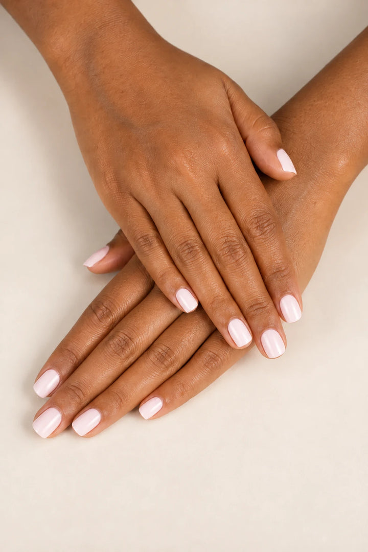 Two hands crossed, showing short, glossy Pink Cloud semi-cured gel nail wraps in a soft milky pink shade against a neutral beige background.