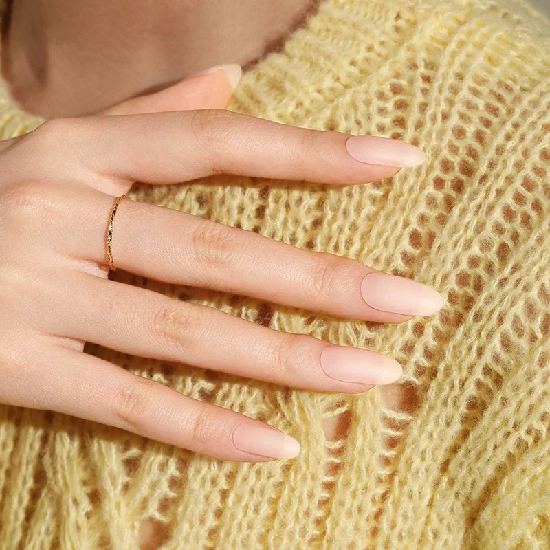 Semi-cured gel nail wraps in a nude-pink shade with a soft matte finish, shown on a hand resting over a yellow knit sweater.