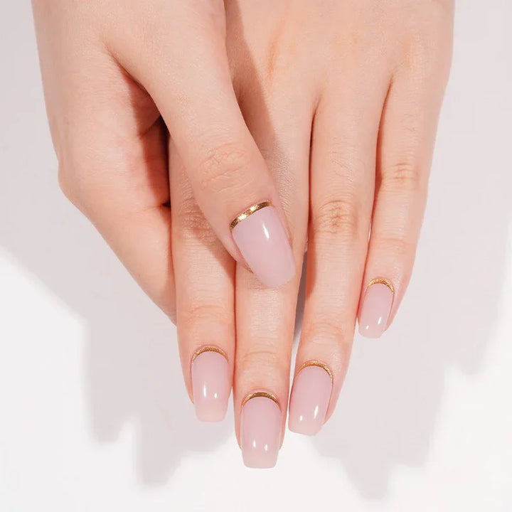 Hands wearing Pink Moon gel nail wraps in glossy nude-pink with gold cuticle cuffs, shown in soft natural lighting.