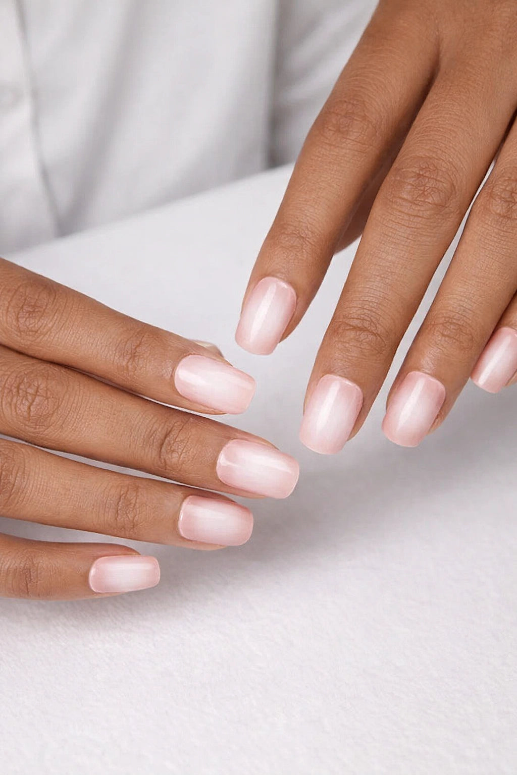 Semi-cured gel nail wraps in soft blush pink with a delicate milky white ombré fade and glossy finish, shown on medium-dark skin against a neutral, white background