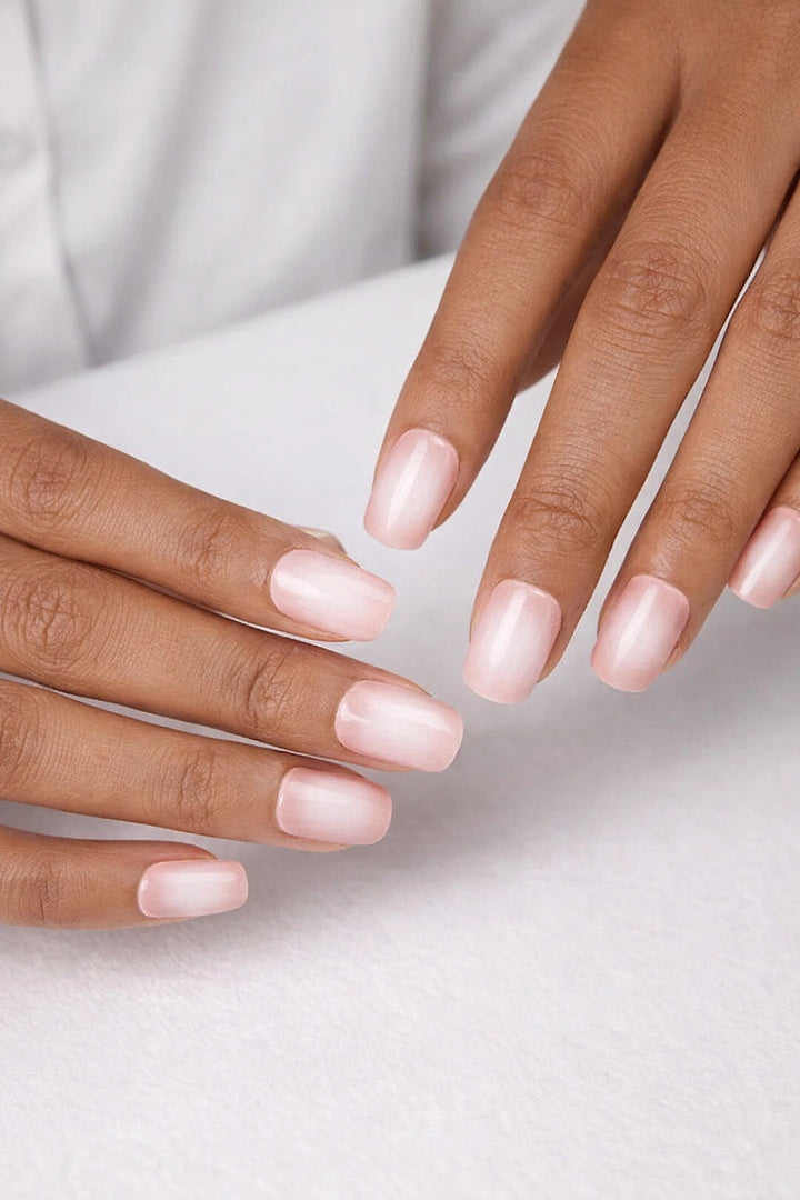 Semi-cured gel nail wraps in soft blush pink with a delicate milky white ombré fade and glossy finish, shown on medium-dark skin against a neutral, white background