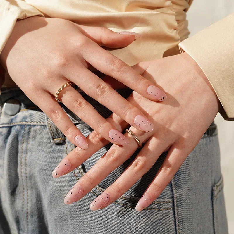Hands wearing Pink Speckled Eggs gel nail wraps in glossy sheer pink with soft black speckles, styled casually against a neutral outfit.