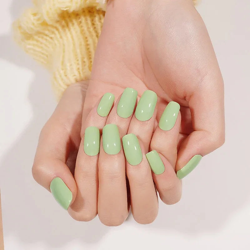 Light-skin hands displaying glossy pistachio-green semi-cured gel nail stickers under soft studio lighting, with a yellow knitted sleeve visible in the background.