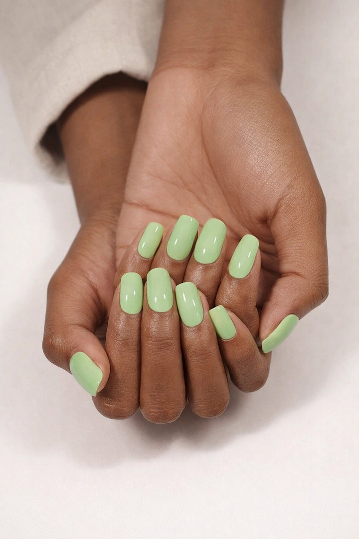 Pistachio semi-cured gel nail stickers, shown on medium-deep brown skin with a soft pistachio-green shade and smooth high-gloss finish, photographed under soft studio lighting against a clean white background.