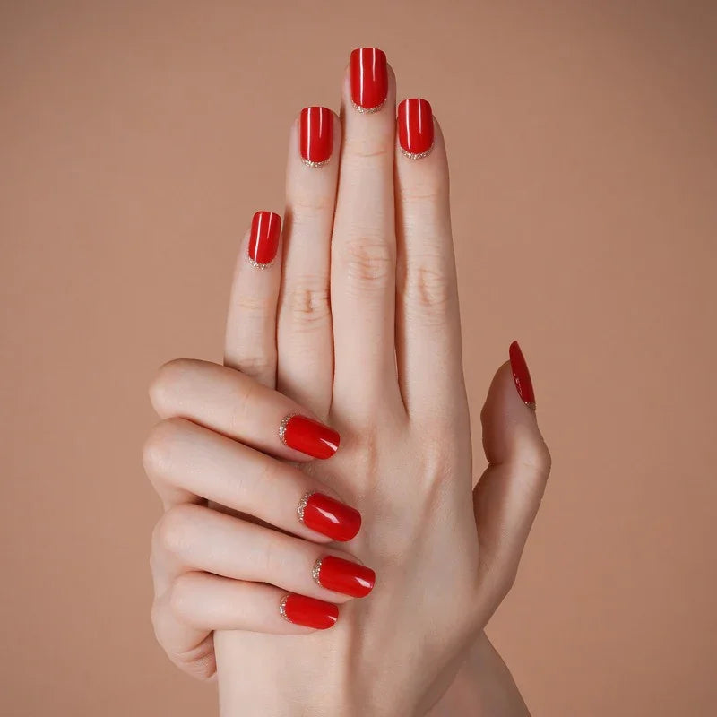 Hands with Red Moon gel nail wraps in a bold, power-red shade featuring golden cuticle cuff accents, shown against a warm neutral background.
