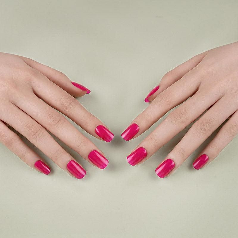 Hands with rich mauve gel nail wraps resting on a muted green surface under soft lighting.