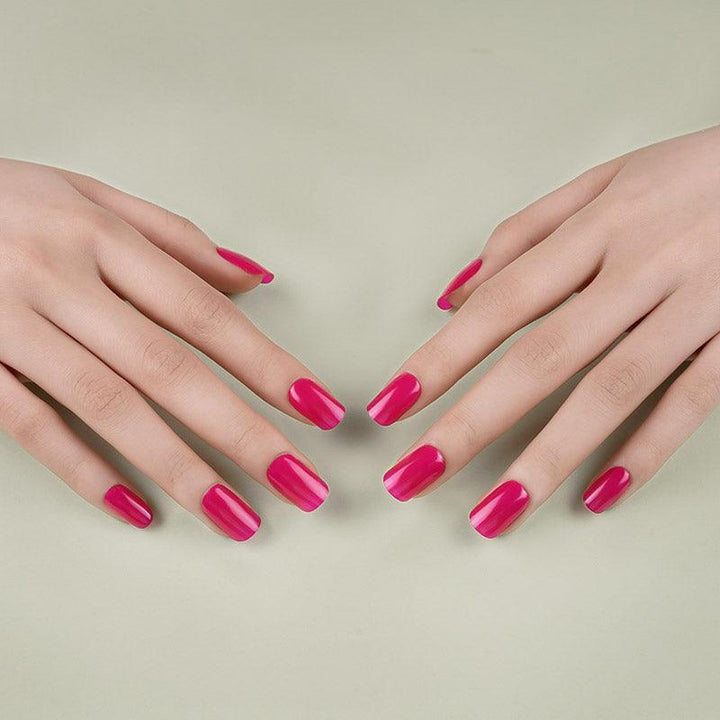 Hands with rich mauve gel nail wraps resting on a muted green surface under soft lighting.