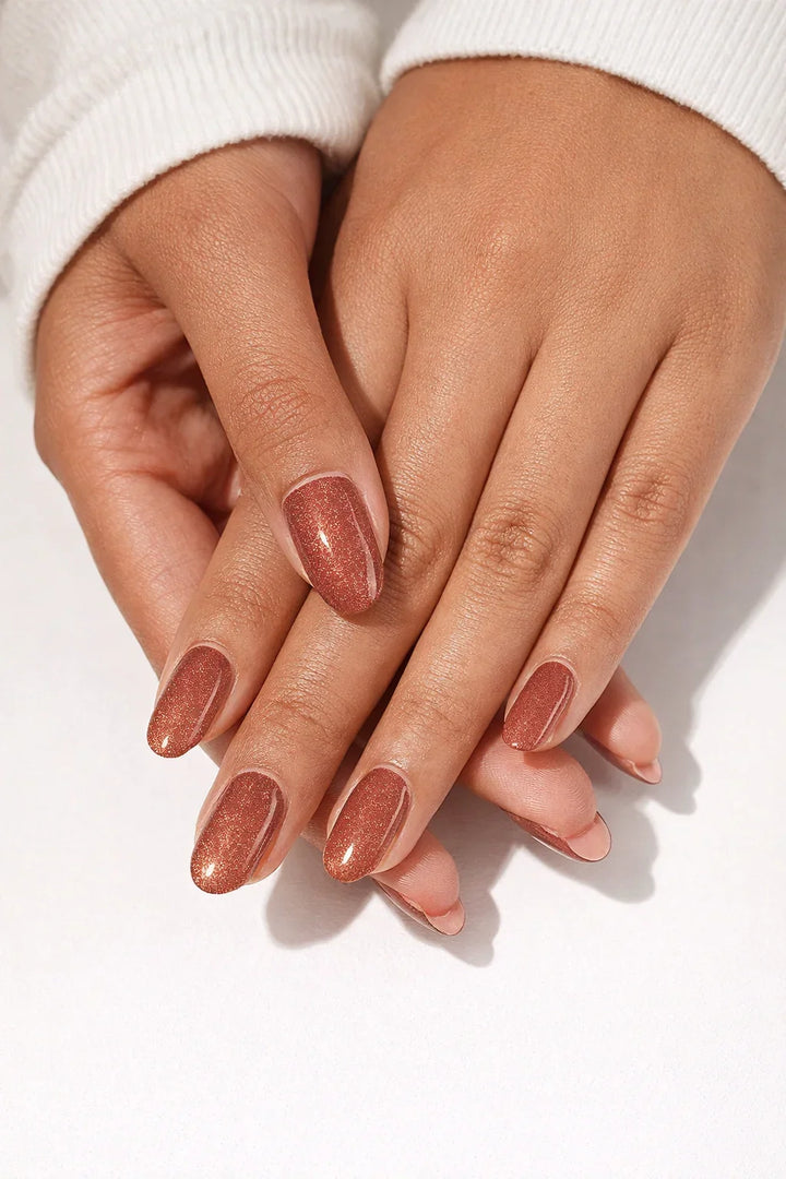 Semi-cured gel nail wraps in warm brick-red with fine magnetic shimmer and a glossy cat-eye finish, shown on medium-dark skin.