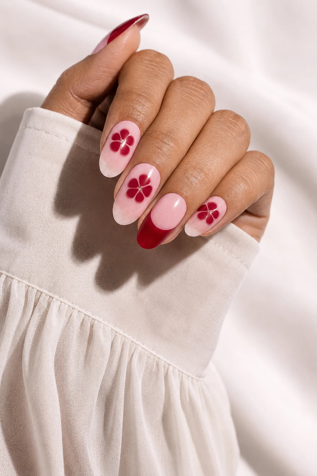 UV-free gel nail wraps in a pink floral Sakura design with deep red accents on medium-brown skin, styled with a cream blouse.