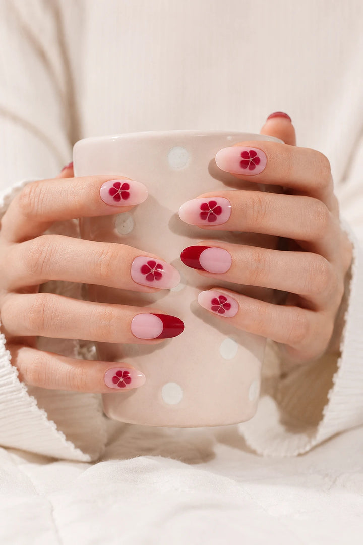 UV-free gel nail wraps in a pink and red floral Sakura design on light skin, styled with cream clothing and a ceramic mug.