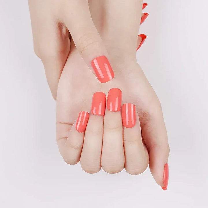 Semi-cured gel nail wraps in bright coral-pink with a glossy finish, shown on light skin with neatly shaped nails.