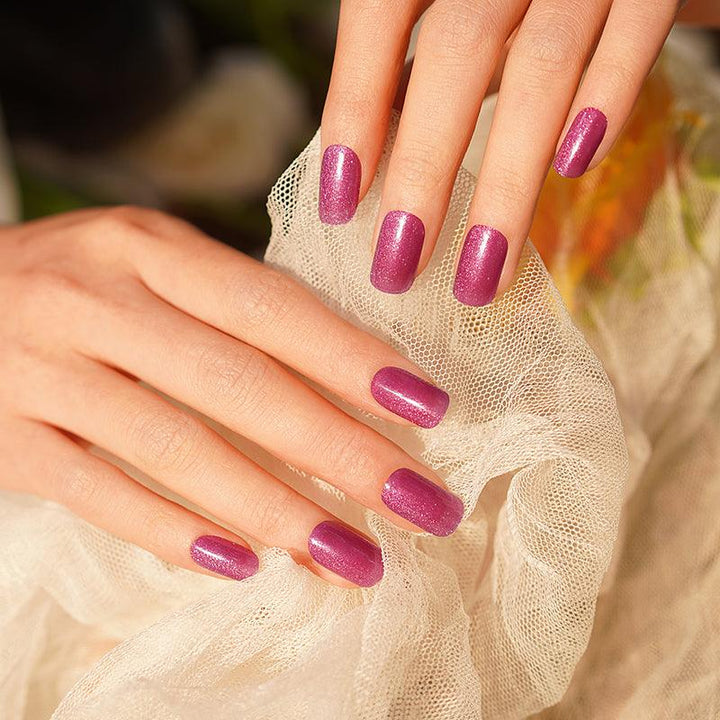 Vibrant magenta gel nails with subtle shimmer and glossy, slightly sheer shine. Photographed in soft light on warm-toned fabric.
