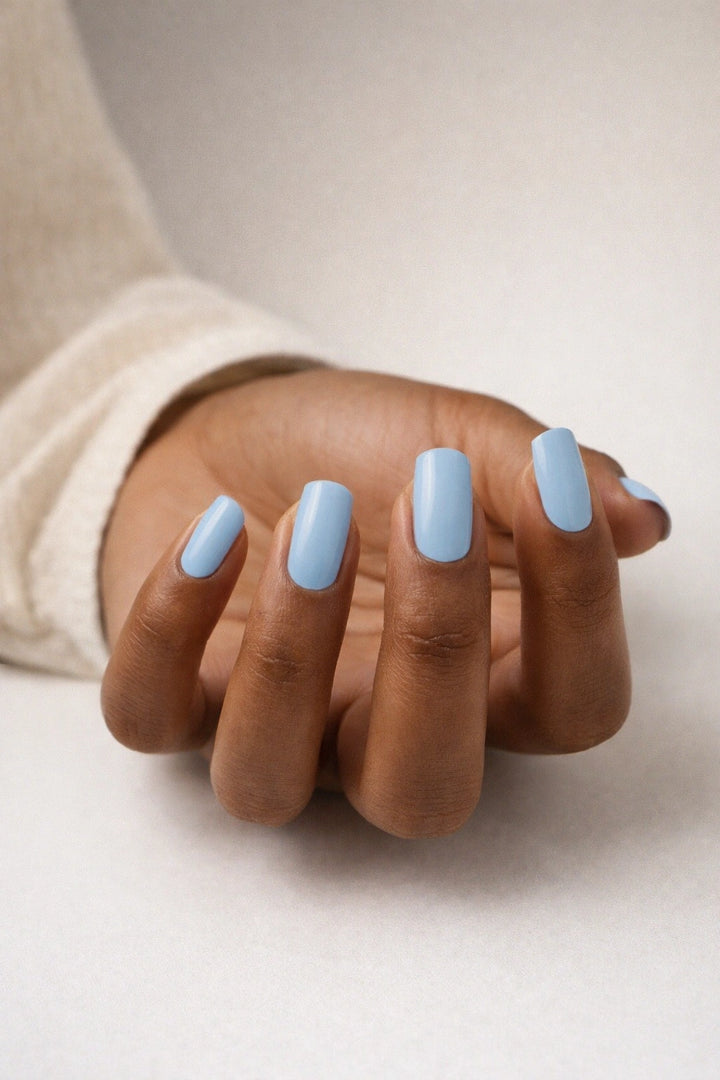Sky Blue semi-cured gel nail stickers, shown on medium-brown skin with a soft pastel blue shade and smooth glossy finish, photographed under soft studio lighting against a clean neutral background.
