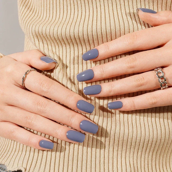 Slate Blue semi-cured gel nail stickers in a muted blue-grey shade with a glossy finish, shown under soft studio lighting on light skin with silver rings and a beige ribbed top.