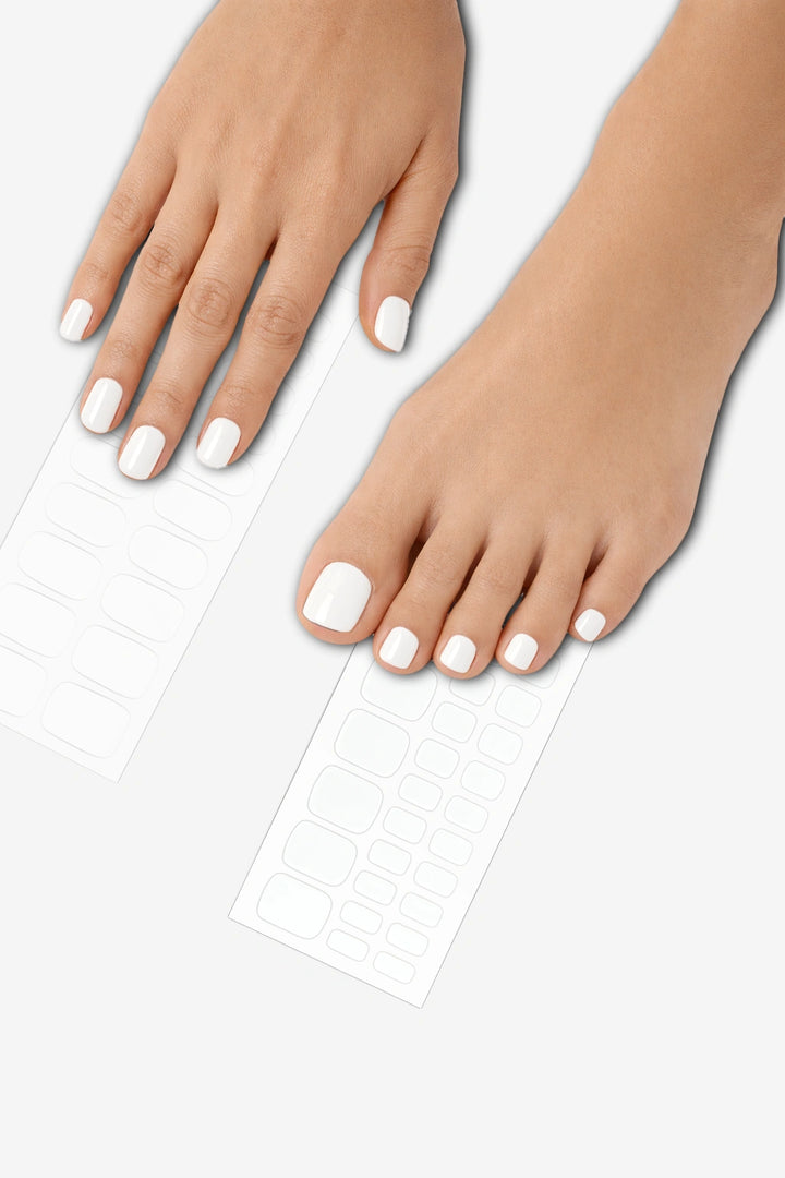 Snow white semi-cured gel nail wrap mani and pedi bundle applied on hands and feet, featuring a glossy solid white finish with matching wrap sheets displayed underneath.