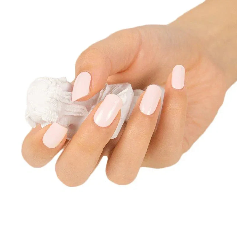 Hand with neatly manicured nails wearing soft pink semi-cured gel nail wraps, holding a small white sculpted object.