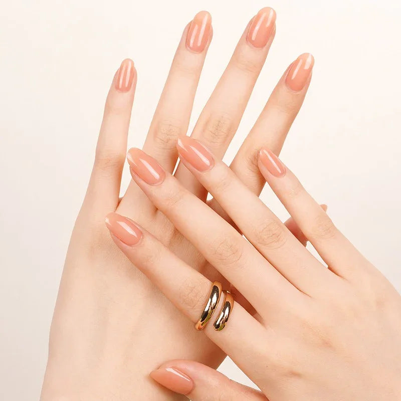 Semi-cured gel nail wraps in peachy orange-pink with a soft translucence and high-gloss shine, shown on fair skin with minimal gold jewelry.