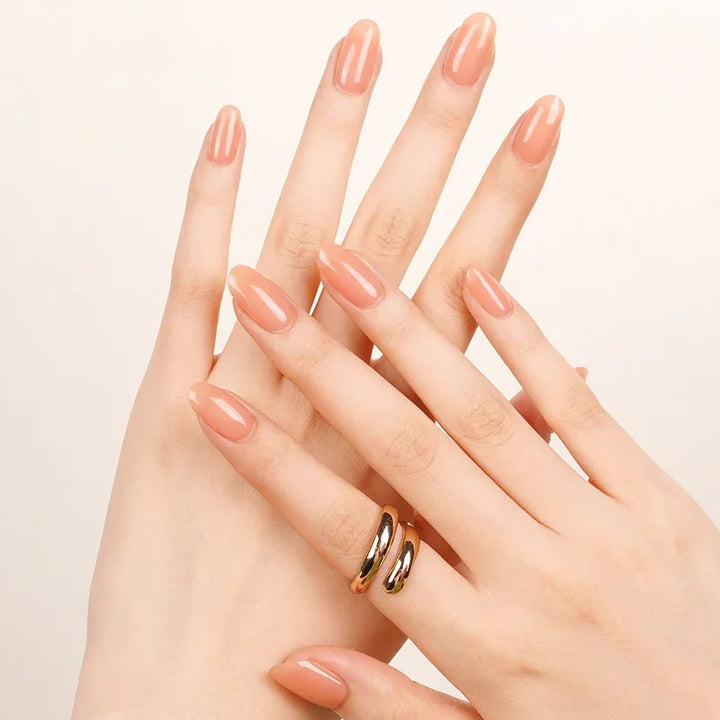 Semi-cured gel nail wraps in peachy orange-pink with a soft translucence and high-gloss shine, shown on fair skin with minimal gold jewelry.