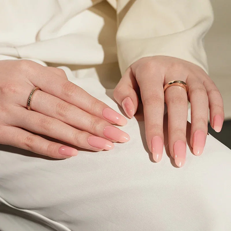 Semi-cured gel nail wraps in soft milky pink with a glossy finish, shown on fair skin wearing a delicate ring and cream outfit.