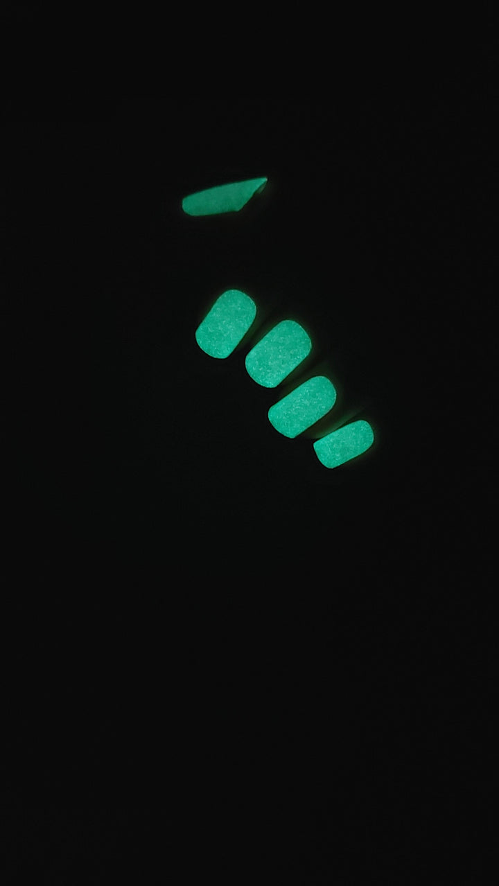 Glow-in-the-dark pink gel nail wraps emitting green light in low-light setting.