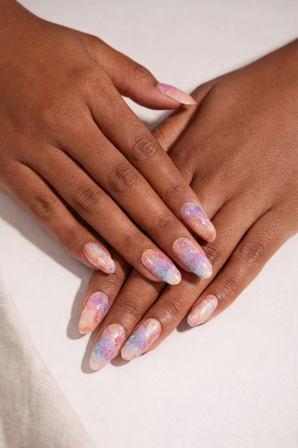 Unicorn Poop semi-cured gel nail stickers, shown on medium-deep brown skin with pastel rainbow swirls, fine shimmer sparkle, and a subtle cat-eye effect, photographed under soft studio lighting against a clean white surface.